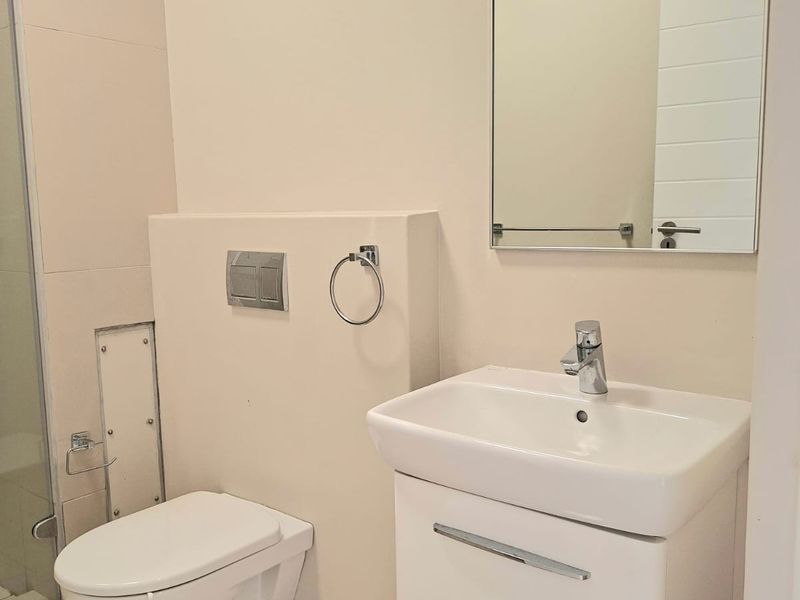 Modern bathroom featuring a wall-hung toilet, vanity cabinet with basin, and a glass shower enclosure with neutral tiled finishes.