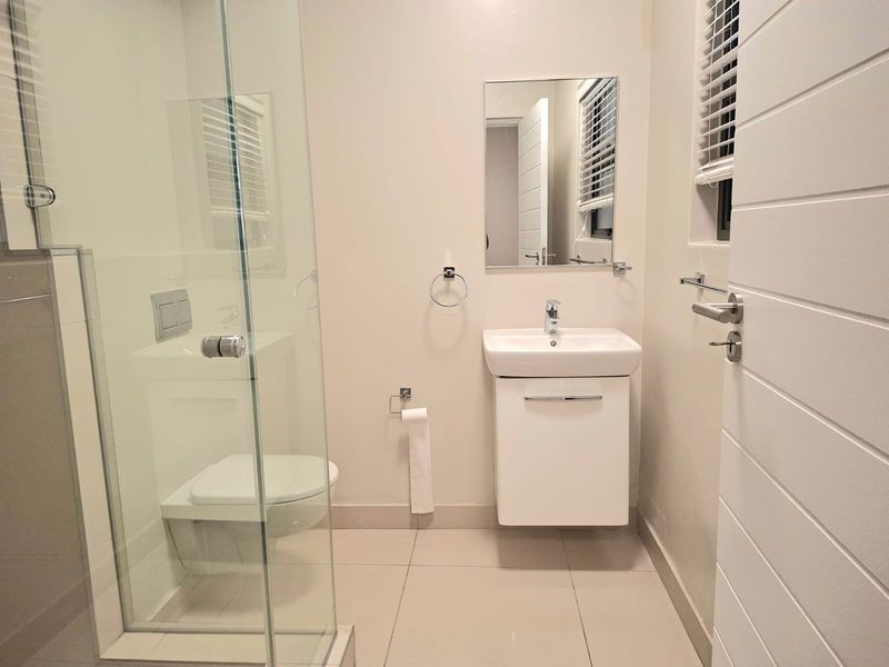 Modern bathroom featuring a glass shower enclosure, wall-mounted vanity with basin, and neutral tiled flooring in excellent condition.