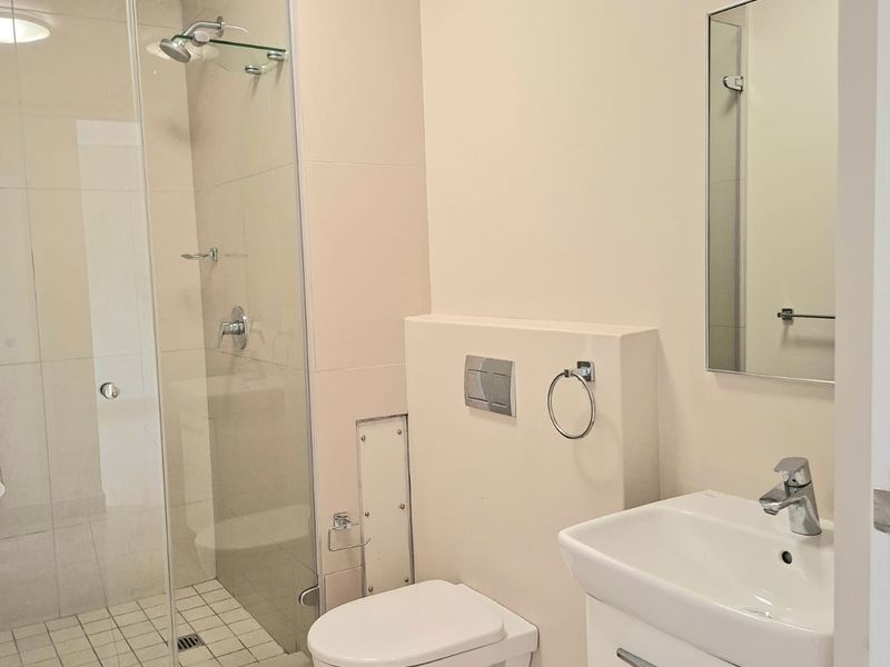 A clean, modern bathroom featuring a glass-enclosed shower, wall-mounted toilet, and a sleek vanity basin with neutral tiling throughout.