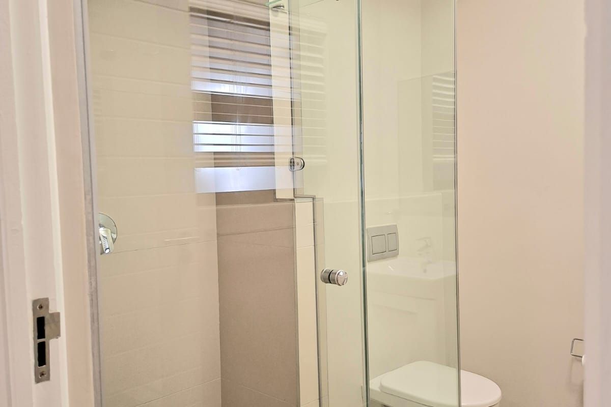 A modern, clean bathroom featuring a glass-enclosed shower, wall-mounted toilet with a concealed cistern, and neutral tiled finishes.