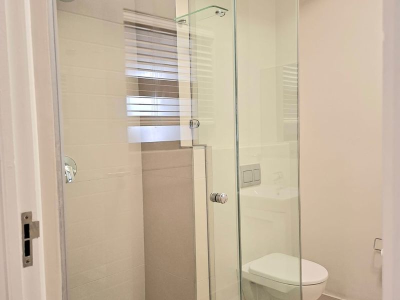 A modern, clean bathroom featuring a glass-enclosed shower, wall-mounted toilet with a concealed cistern, and neutral tiled finishes.