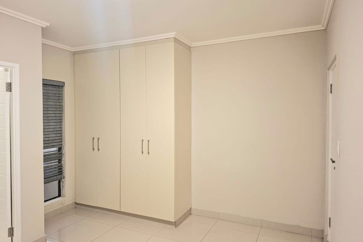 A clean, empty bedroom featuring neutral tiled flooring, built-in cupboards, and window blinds, offering a blank canvas for personalization.