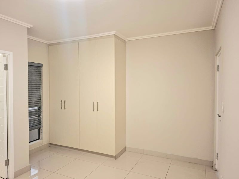 A clean, empty bedroom featuring neutral tiled flooring, built-in cupboards, and window blinds, offering a blank canvas for personalization.