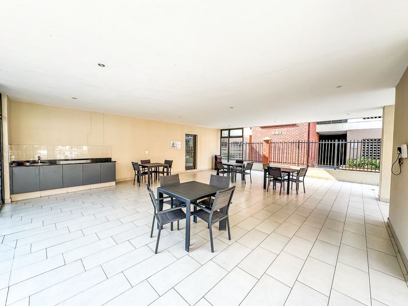 Spacious covered outdoor clubhouse area featuring tiled flooring, a built-in kitchenette with sink, and ample space for communal seating and social gatherings.