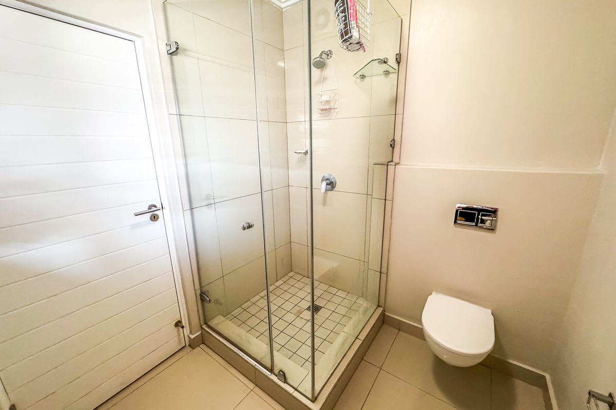 A clean, modern bathroom featuring a glass-enclosed shower, wall-mounted toilet with chrome flush plate, and neutral floor tiling.