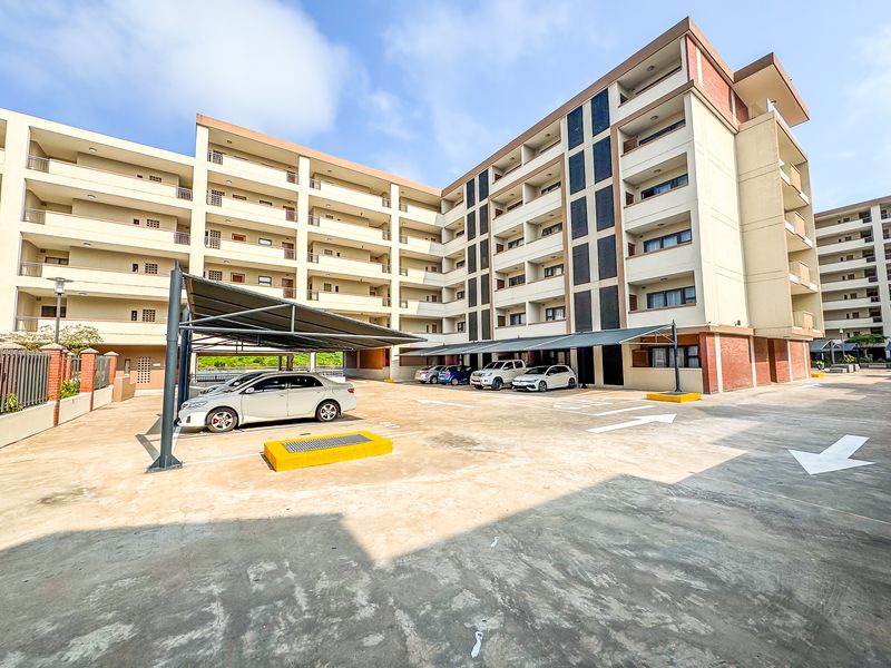 Exterior view of a multi-story apartment complex featuring covered parking bays and paved driveway areas.