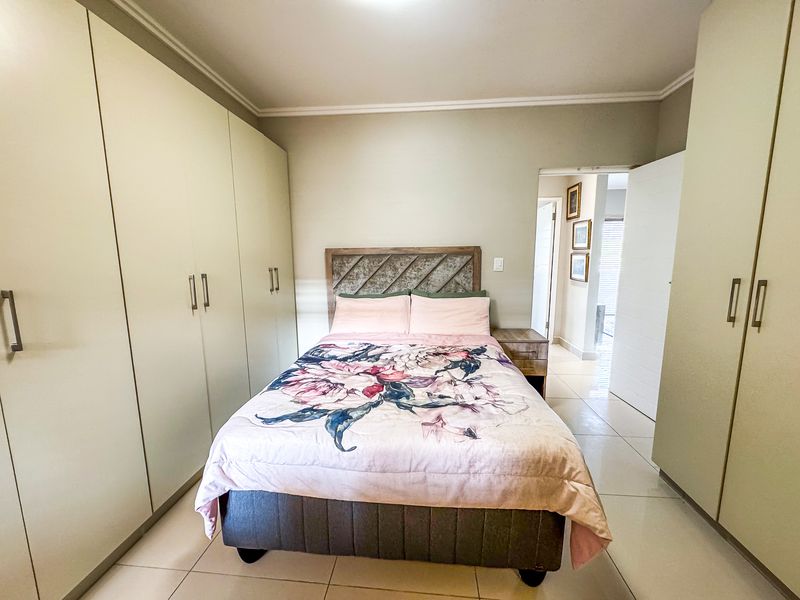 A well-maintained bedroom featuring extensive built-in cupboards, neutral tiled flooring, and coved ceiling details, offering a clean and functional living space.