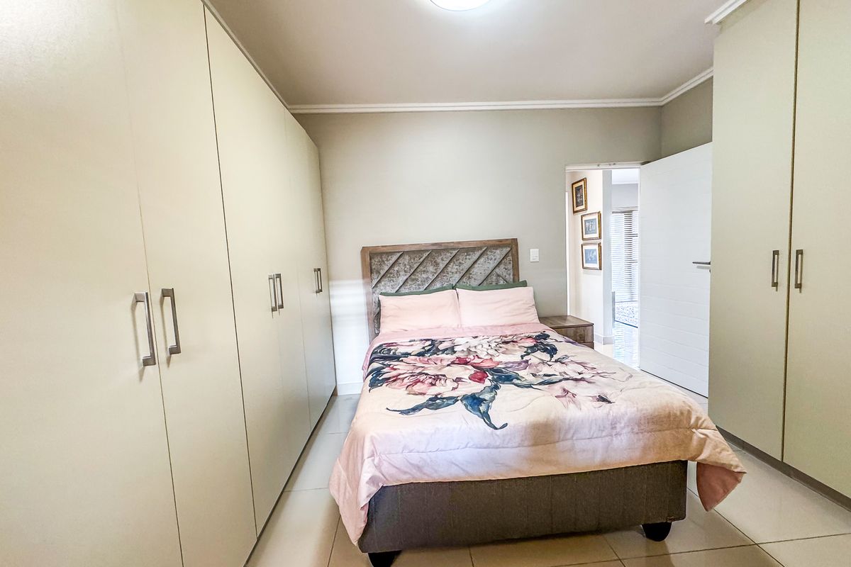 A well-maintained bedroom featuring extensive built-in cabinetry, neutral tiled flooring, and clean finishes, offering ample storage space.