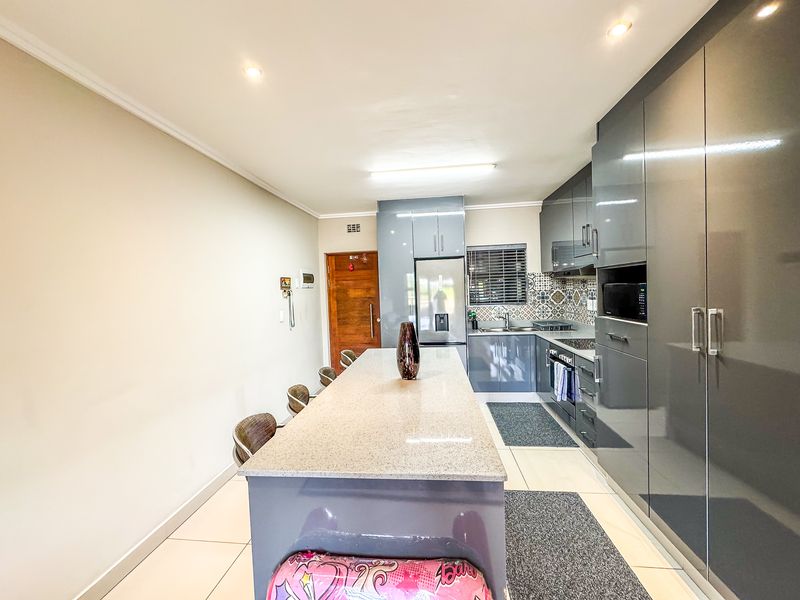 Modern kitchen featuring high-gloss grey cabinetry, a central stone-topped island, integrated appliances, and a stylish patterned tile backsplash.