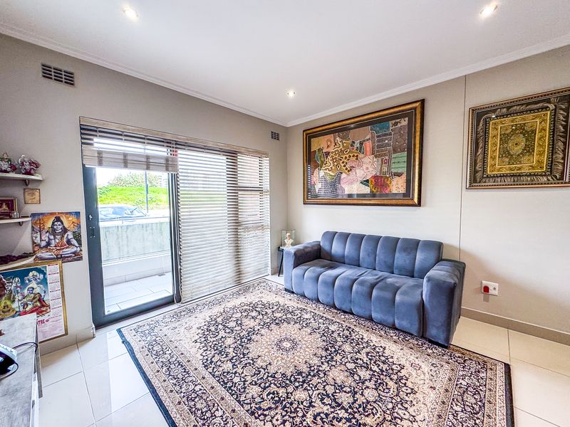 A bright living room featuring tiled flooring, recessed downlights, and a large sliding glass door providing access to an outdoor balcony area.