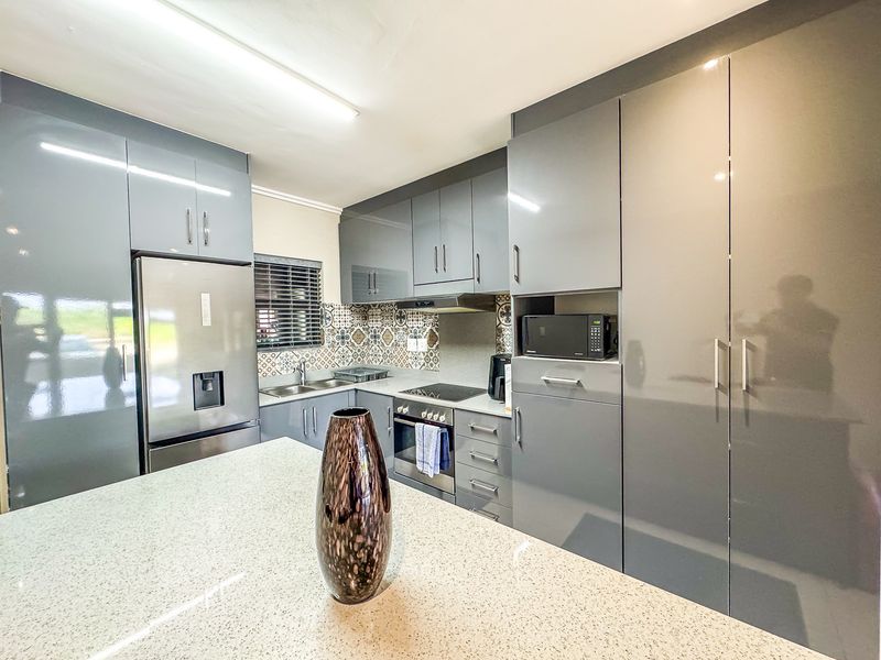 Modern kitchen featuring high-gloss grey cabinetry, stone countertops, patterned tile backsplash, and integrated appliances including an oven, cooktop, and microwave.