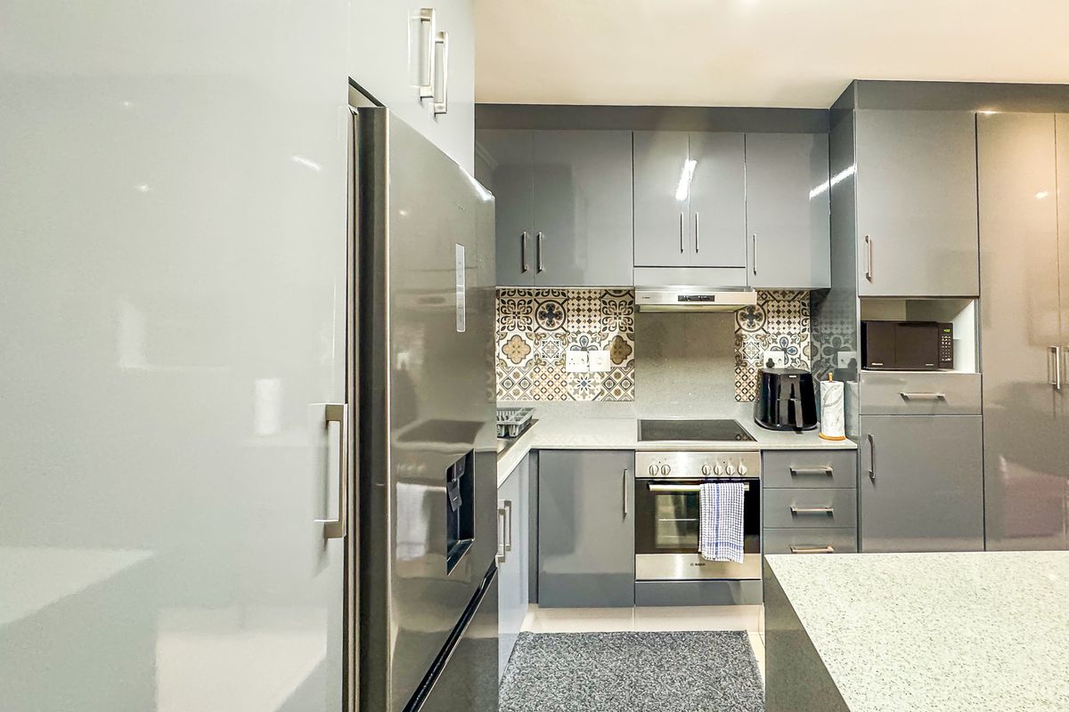 Modern kitchen featuring high-gloss grey cabinetry, patterned tile backsplash, stone countertops, and integrated stainless steel appliances.