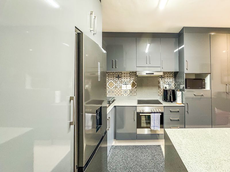 Modern kitchen featuring high-gloss grey cabinetry, patterned tile backsplash, stone countertops, and integrated stainless steel appliances.