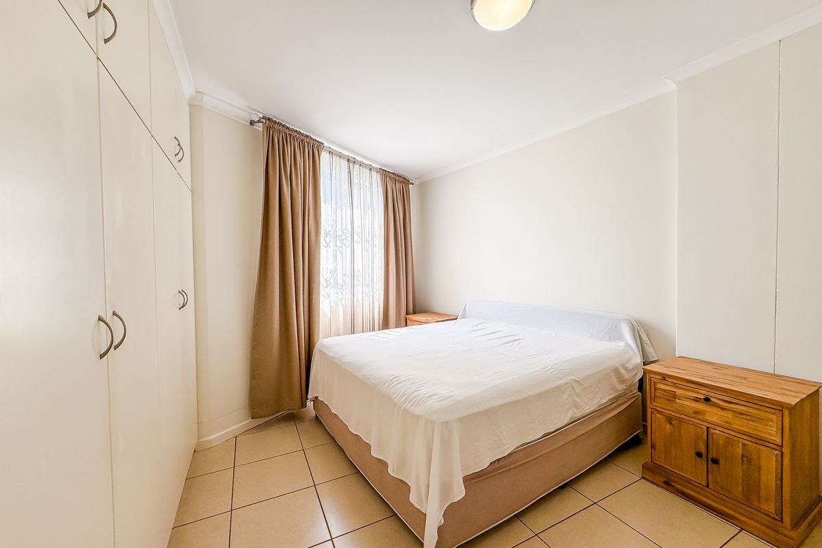 A functional bedroom featuring neutral tiled flooring, built-in storage cupboards, and natural light through window curtains.