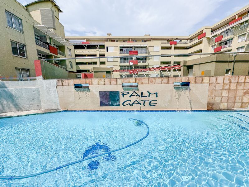 Communal swimming pool area at Palm Gate apartment complex featuring a decorative water feature and glass balustrade.