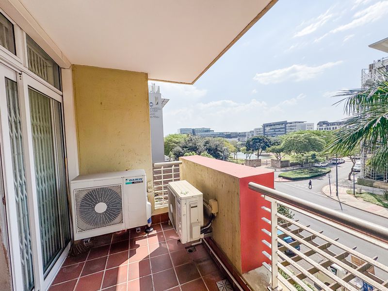 A balcony featuring tiled flooring, metal railings, and dual air conditioning condenser units, offering an elevated view of the surrounding urban landscape.