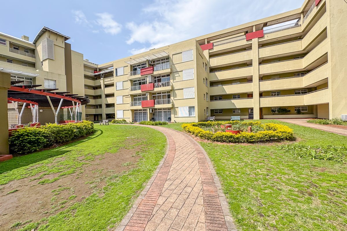 A view of the apartment complex exterior featuring a paved walkway, landscaped garden areas, and multi-level balconies.
