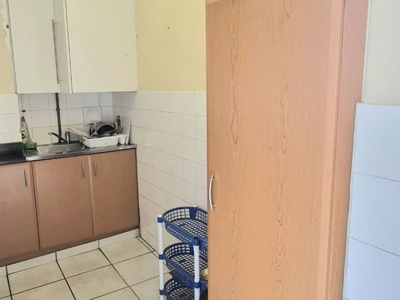 A compact kitchen area featuring built-in cabinetry, a stainless steel sink, and tiled finishes, requiring some cosmetic updates to improve its overall appeal.