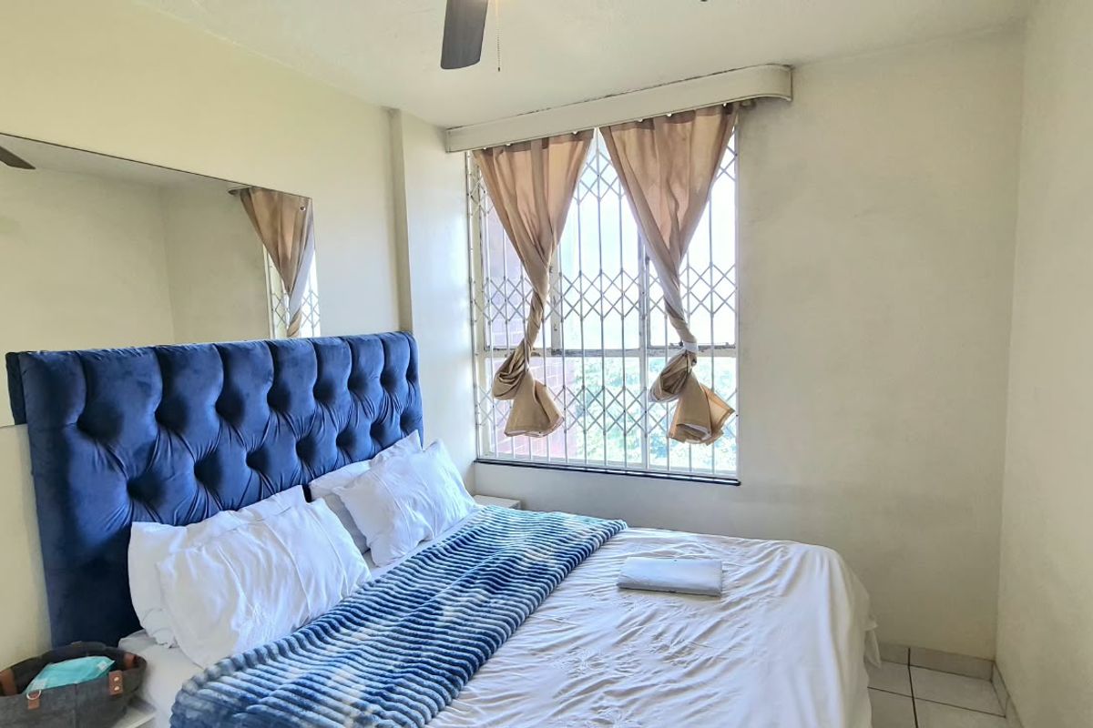 A bedroom featuring tiled flooring, a ceiling fan, and a window fitted with a security gate, offering a functional living space.