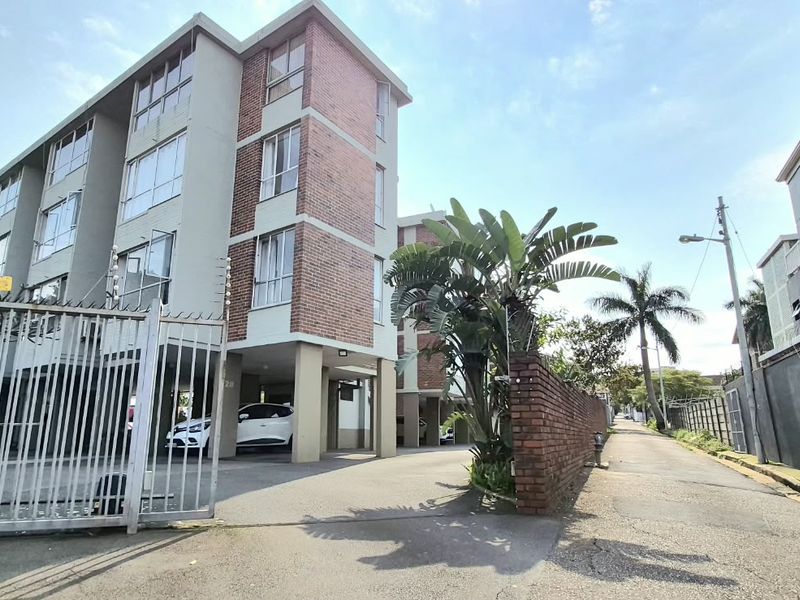 Exterior view of an apartment complex featuring a paved driveway, covered parking, and secure gated access with perimeter electric fencing.