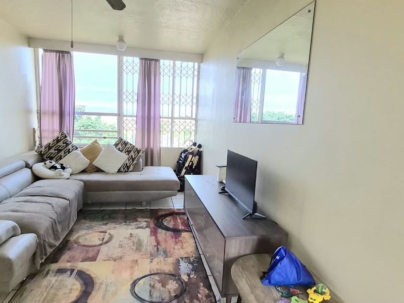 A functional living room featuring a large window with security bars, a ceiling fan, and a wall-mounted mirror.