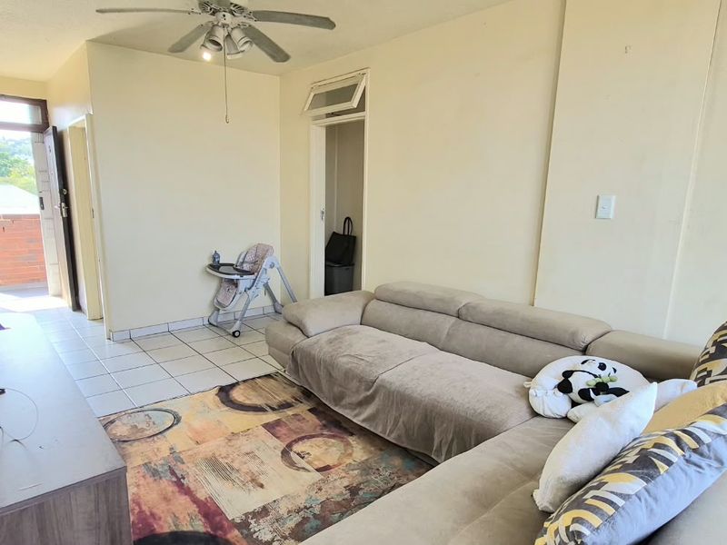 A living room featuring tiled flooring, a ceiling fan, and access to an outdoor balcony area.