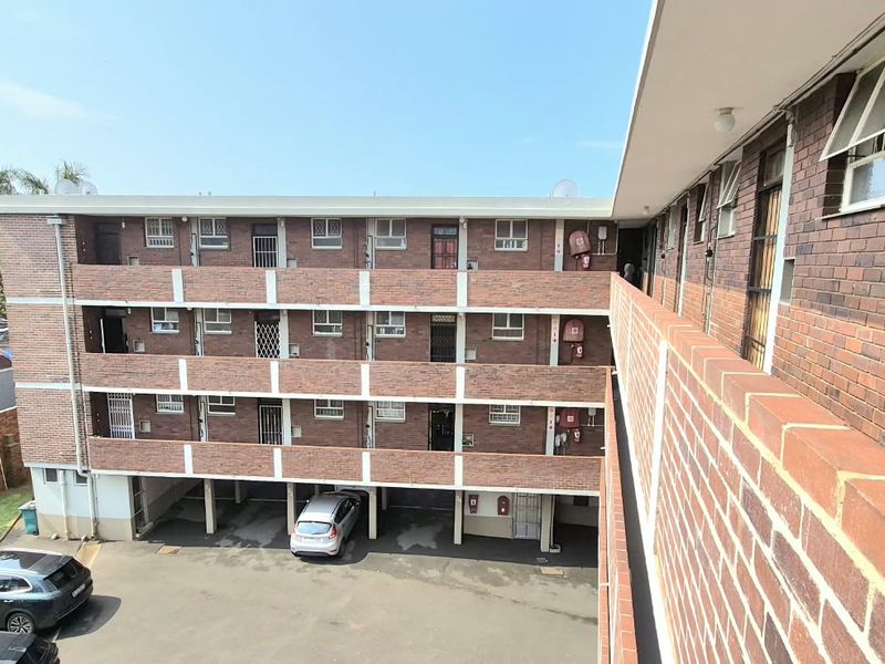 Exterior view of a multi-story brick apartment complex featuring open-air walkways, security gates, and ground-level covered parking facilities.