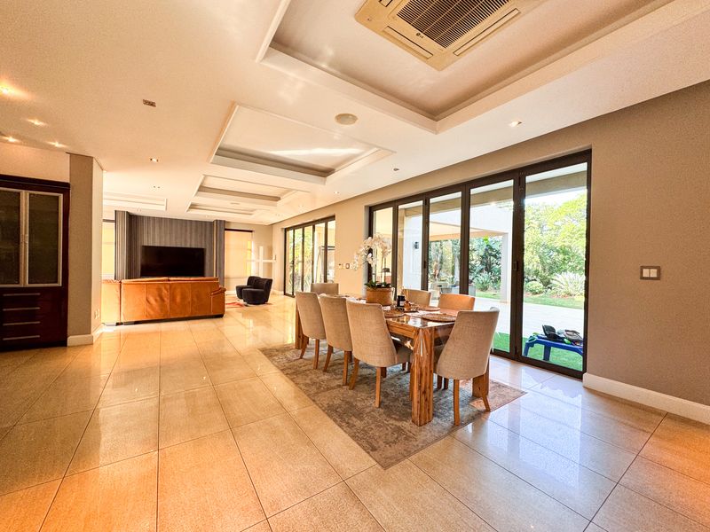 Spacious open-plan living and dining area featuring high-gloss tiled floors, recessed ceiling details, ducted air conditioning, and large sliding doors opening to the garden.