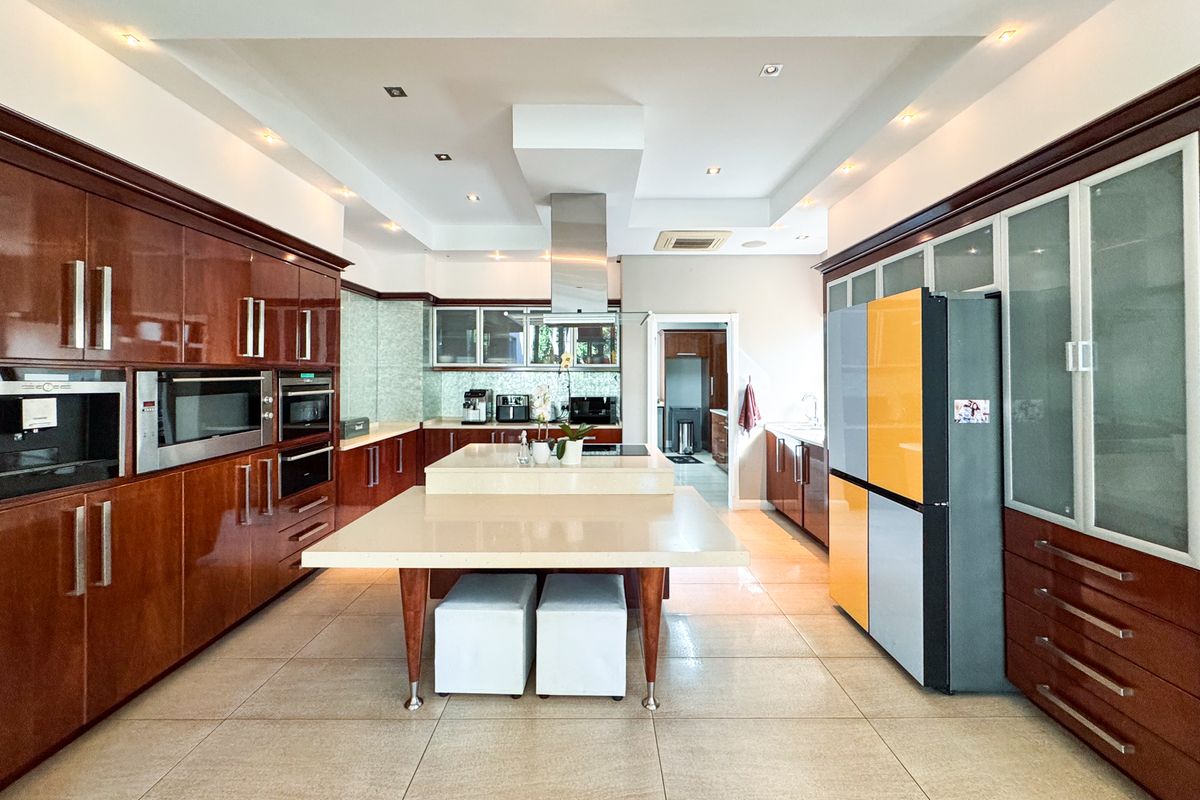 Spacious kitchen featuring extensive dark wood cabinetry, a large central island with stone countertops, integrated appliances, and modern recessed ceiling lighting.
