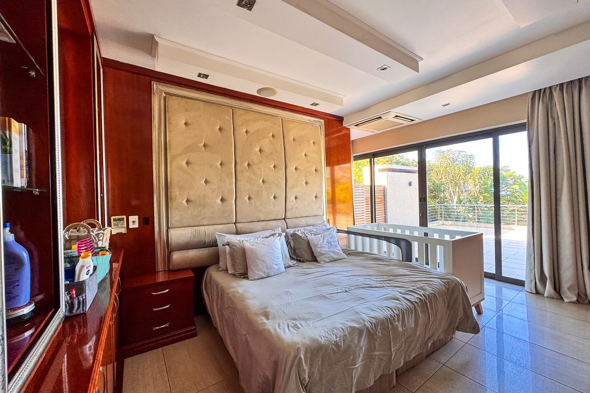 Spacious bedroom featuring built-in cabinetry, a large upholstered headboard, recessed ceiling lighting, and sliding glass doors leading to an outdoor balcony.