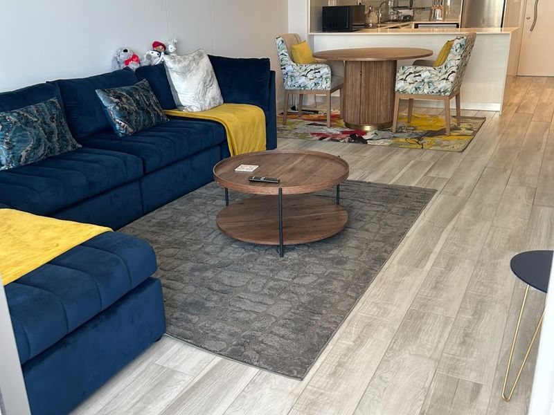 A modern open-plan living and dining area featuring light wood-look tiled flooring, recessed lighting, and a sleek, well-maintained kitchen with built-in cabinetry.