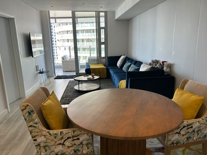 An open-plan living and dining area featuring modern tiled flooring, recessed lighting, and large sliding glass doors leading to a private balcony.