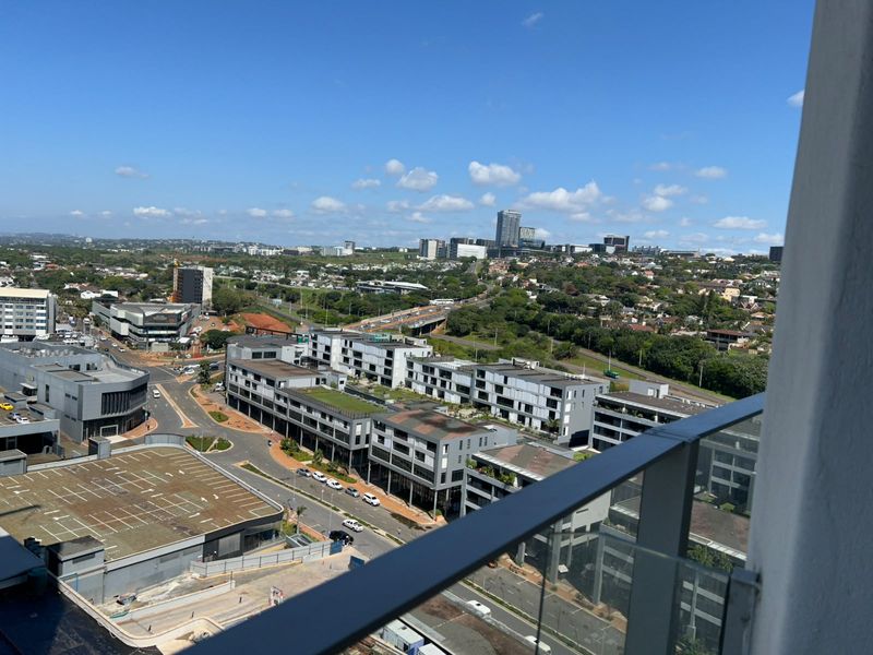 Elevated urban view overlooking the surrounding neighborhood and commercial district, captured from a balcony with a modern glass balustrade.