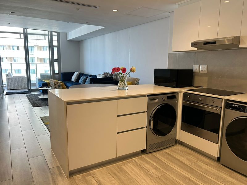 Modern open-plan apartment featuring a sleek kitchen with integrated appliances, stone countertops, and seamless flow to the living area and balcony.