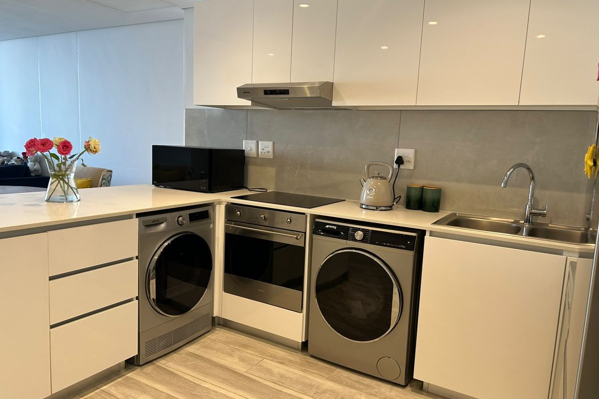 Modern kitchen featuring sleek white cabinetry, stone countertops, integrated appliances including a washing machine and dryer, and a contemporary tiled splashback.