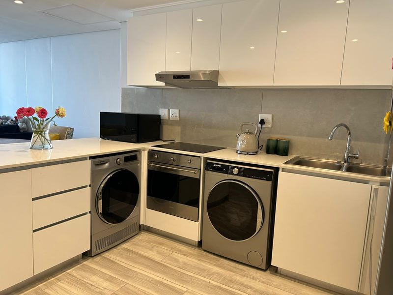Modern kitchen featuring sleek white cabinetry, stone countertops, integrated appliances including a washing machine and dryer, and a contemporary tiled splashback.