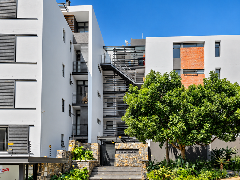 Modern apartment complex facade featuring stone cladding, clean architectural lines, metal staircases, and secure gated entrance with established landscaping.