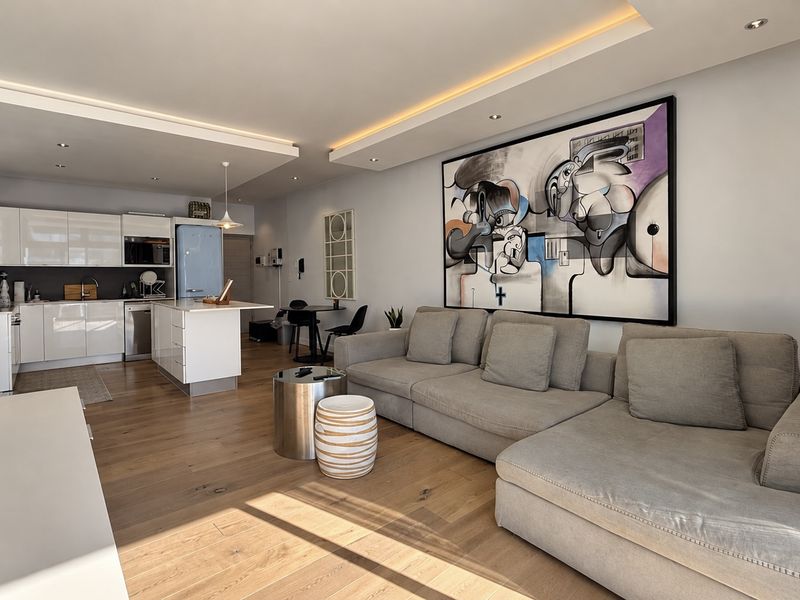 Modern open-plan living area featuring high-quality hardwood flooring, recessed cove lighting, and a sleek, contemporary kitchen with integrated appliances.