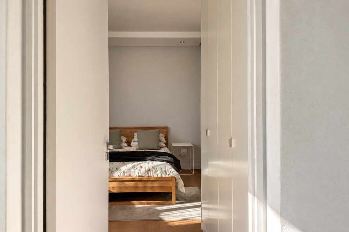 A view through a doorway into a bedroom featuring built-in cupboards, recessed ceiling lighting, and warm laminate flooring.