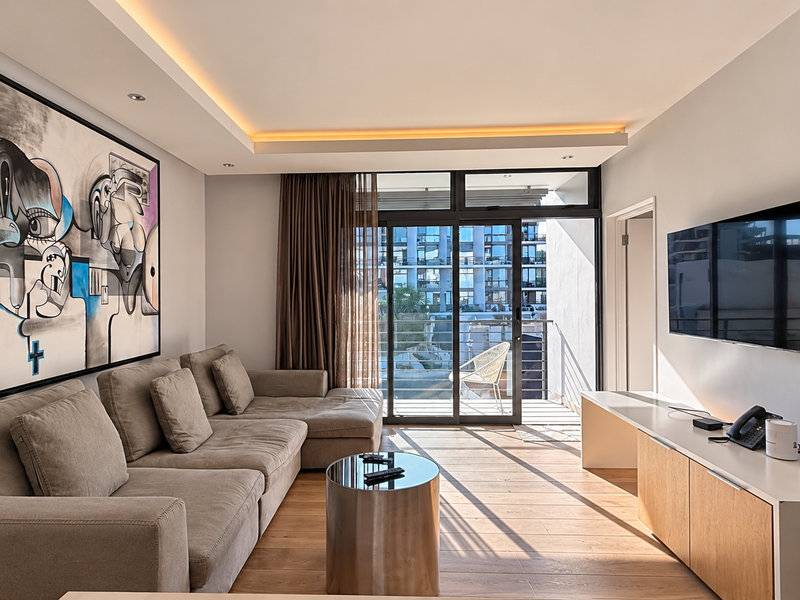 Modern living room featuring hardwood flooring, recessed cove lighting, and large sliding glass doors leading to a private balcony.