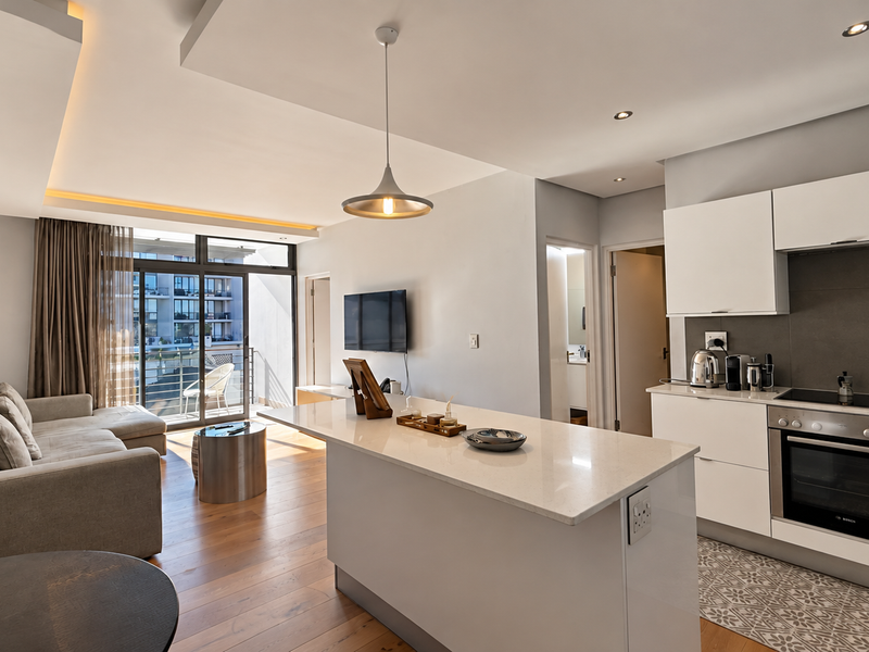 Modern open-plan living area featuring a sleek kitchen with quartz island, built-in appliances, hardwood flooring, and seamless access to a private balcony.