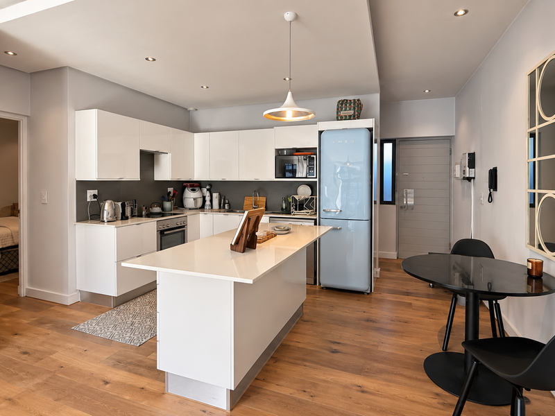 Modern open-plan kitchen featuring white gloss cabinetry, a stone island, and timber flooring, seamlessly integrated into the living space.