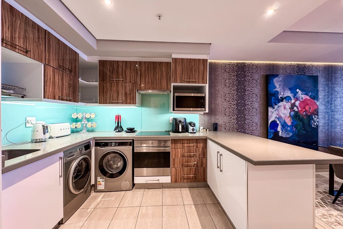 Modern kitchen featuring wood-grain and white cabinetry, stone countertops, glass splashback, integrated appliances, and recessed lighting in an open-plan layout.