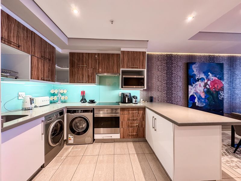 Modern kitchen featuring wood-grain and white cabinetry, stone countertops, glass splashback, integrated appliances, and recessed lighting in an open-plan layout.