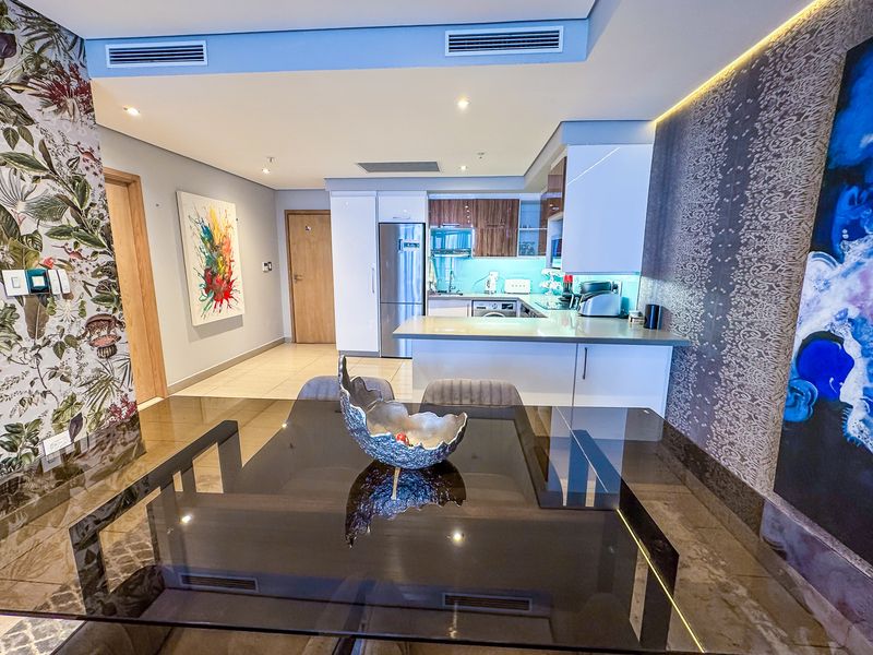 Modern open-plan living and kitchen area featuring sleek cabinetry, stone countertops, integrated appliances, and recessed ceiling lighting in a well-maintained apartment setting.