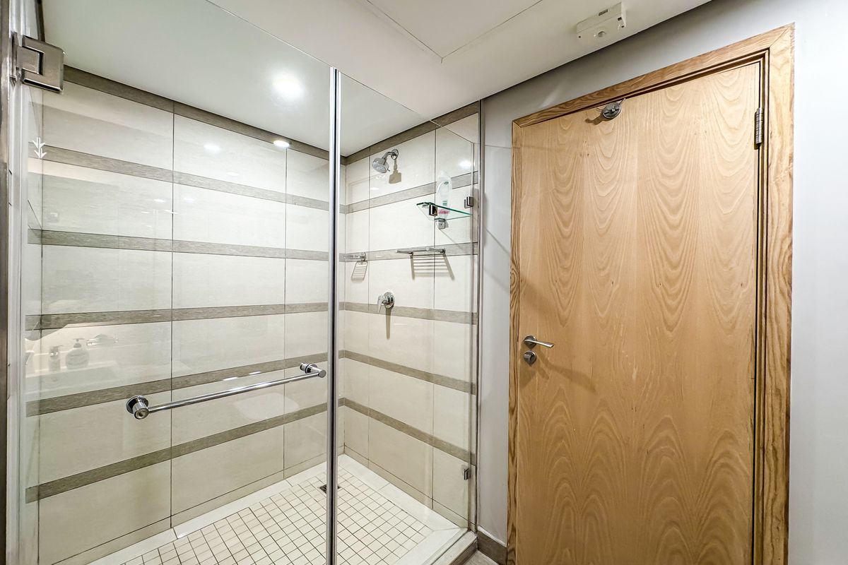 A clean, modern bathroom featuring a glass-enclosed walk-in shower with tiled walls and a wooden door.