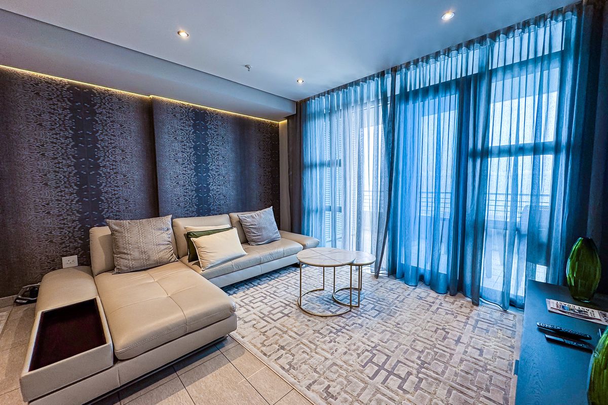 A modern living room featuring tiled floors, recessed cove lighting, and large sliding glass doors that provide access to the balcony.