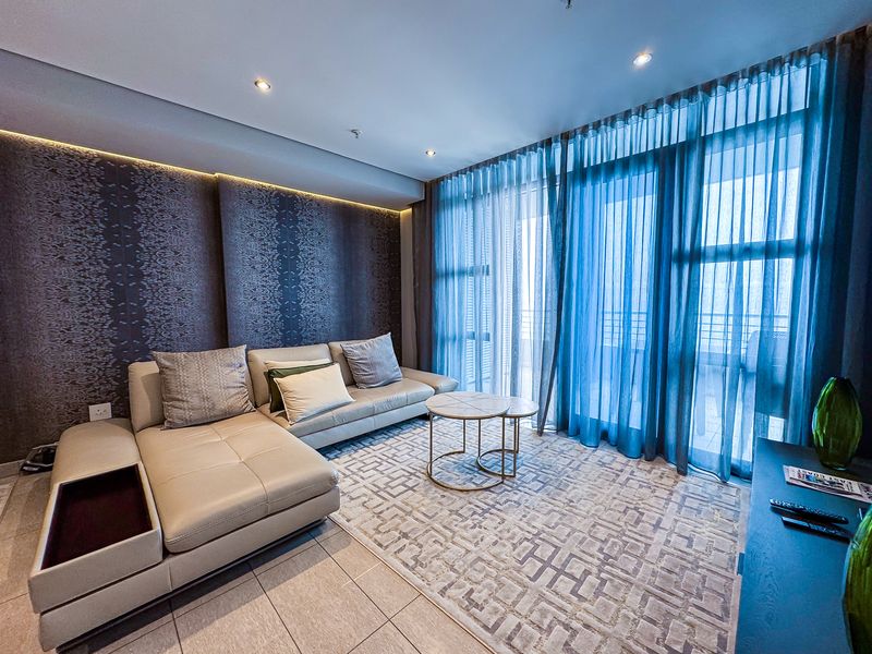 A modern living room featuring tiled floors, recessed cove lighting, and large sliding glass doors that provide access to the balcony.