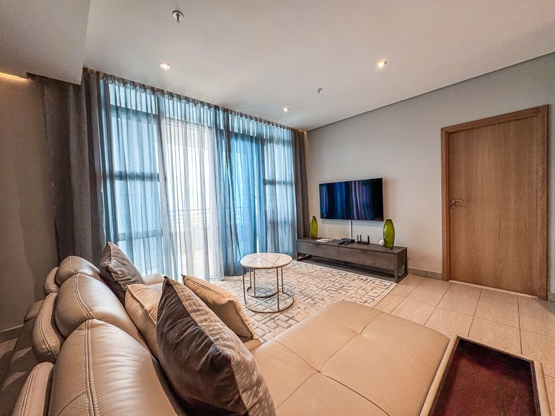 A well-maintained living room featuring tiled flooring, recessed downlights, and large floor-to-ceiling windows that provide ample natural light.