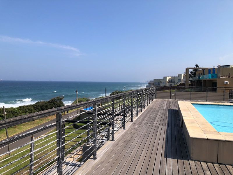 An elevated outdoor pool area featuring timber decking, a metal balustrade, and expansive ocean views.